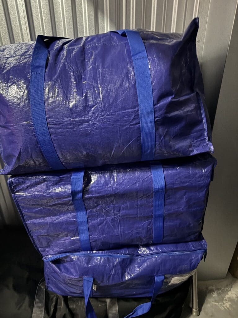 Three large blue reusable storage bags with handles, perfect for college move out organization, are stacked on top of each other in front of a metallic corrugated wall.