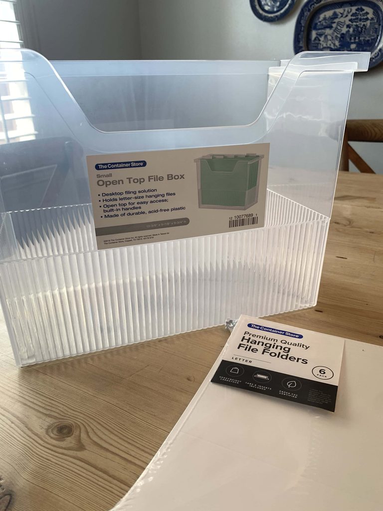 Empty clear Small Open Top File Box from The Container Store on a wood table, next to a 6-pack of letter-size hanging file folders.